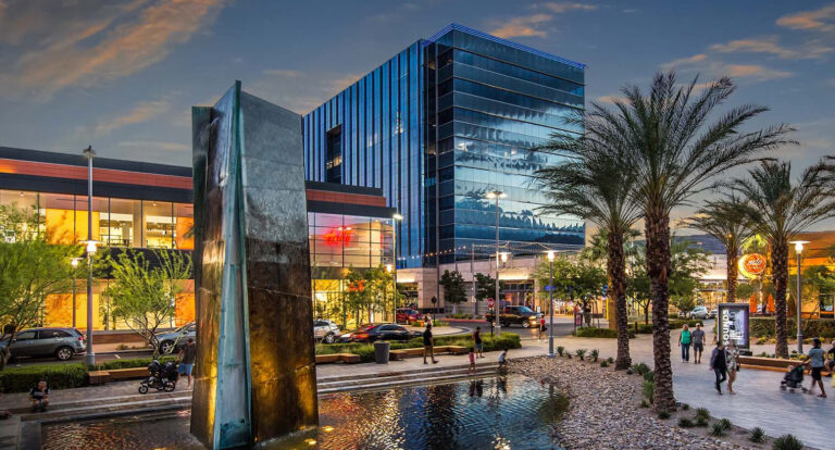 A city fountain surrounded by palm trees, with a modern building in the background, showcasing urban beauty and tranquility.