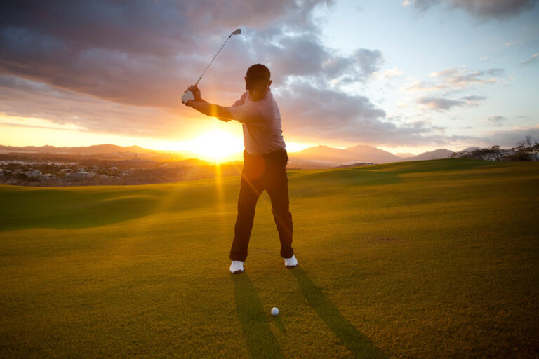 A golfer takes a swing as the sun sets.