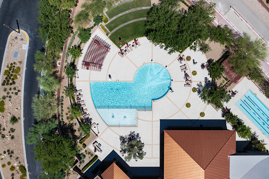 Aerial view of a public space with a pool, walkways, greenery, and scattered seating areas.