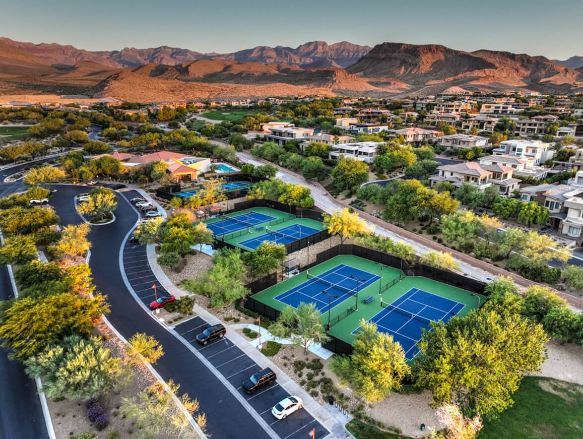 Aerial view of a tennis court surrounded by arid desert landscape, showcasing vibrant colors against the sandy terrain.