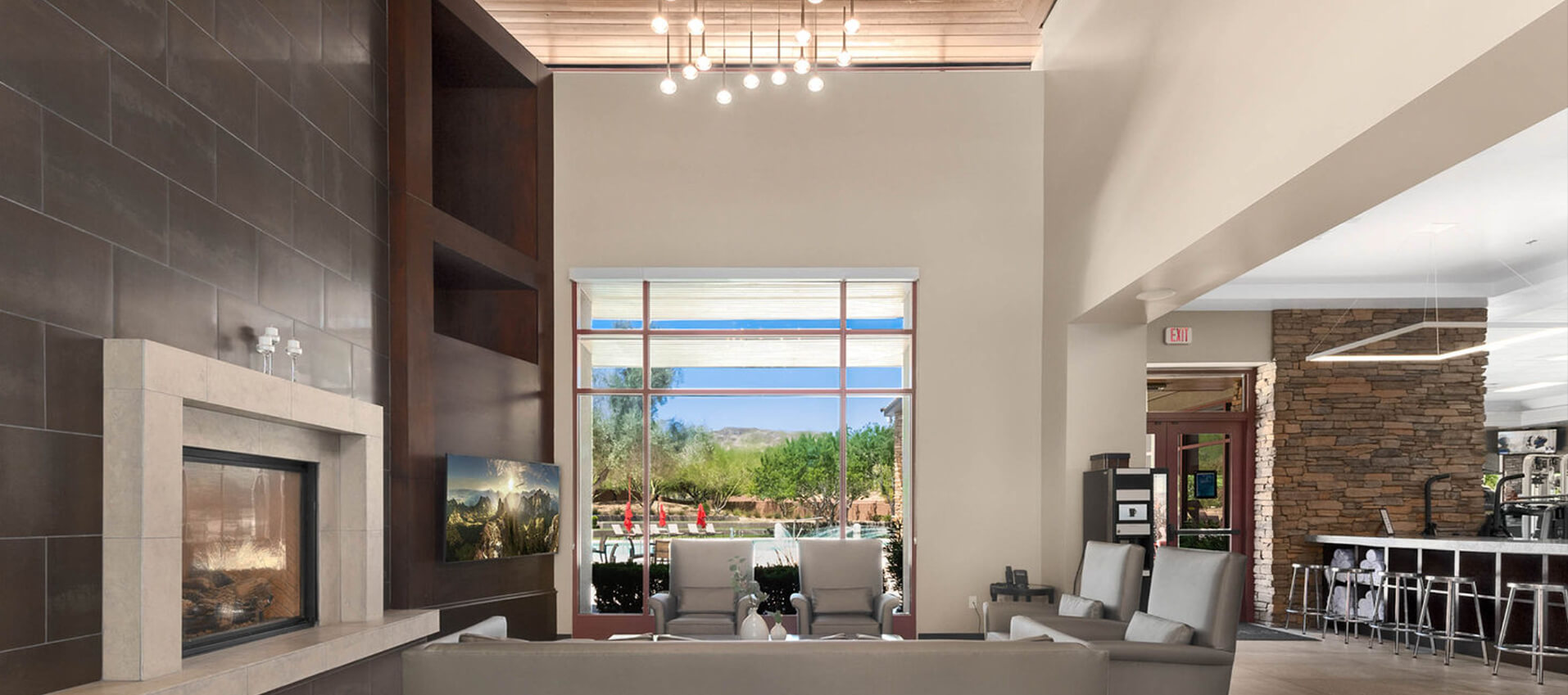 Modern room with fireplace, sofas, large window overlooking patio, and hanging lights.