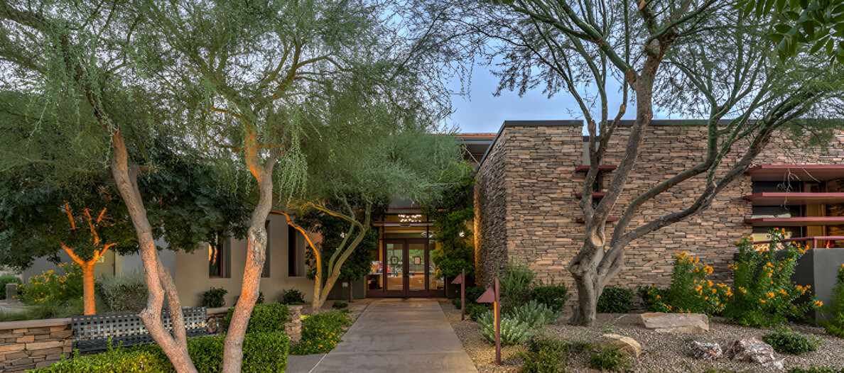 Pathway leading to a building, flanked by green trees and landscaped garden.