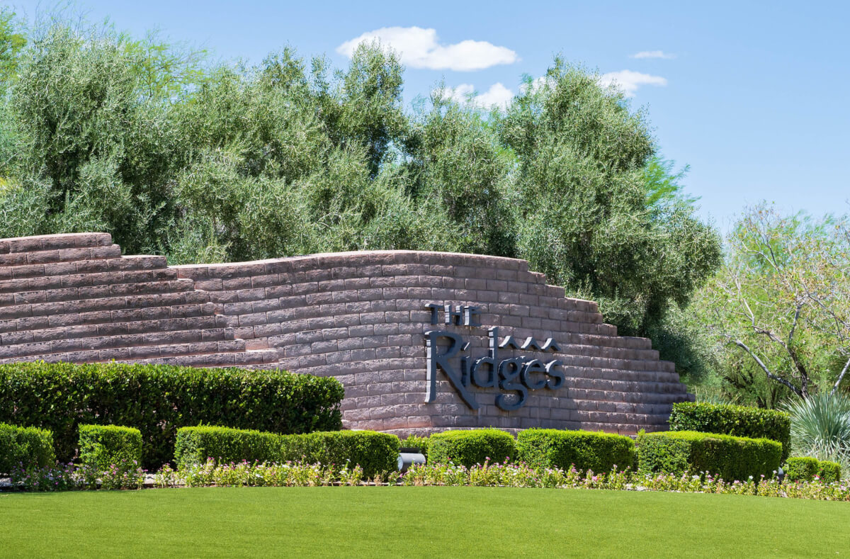 "The Ridges" sign with green foliage and a clear blue sky in the background.